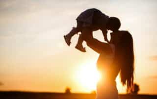 Domestic violence and impact on child custody in the state of Maine portrayed by a mother holding her child up in a setting sun.