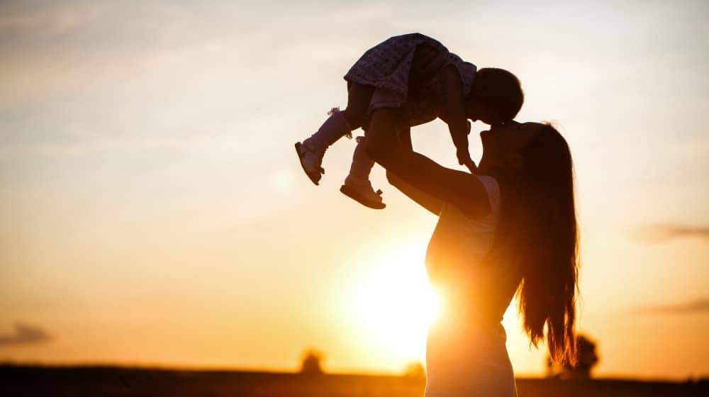 Domestic violence and impact on child custody in the state of Maine portrayed by a mother holding her child up in a setting sun.